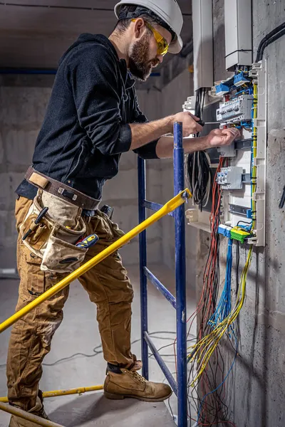 Um eletricista masculino trabalha em um quadro com um cabo de conexão elétrica . — Fotografia de Stock