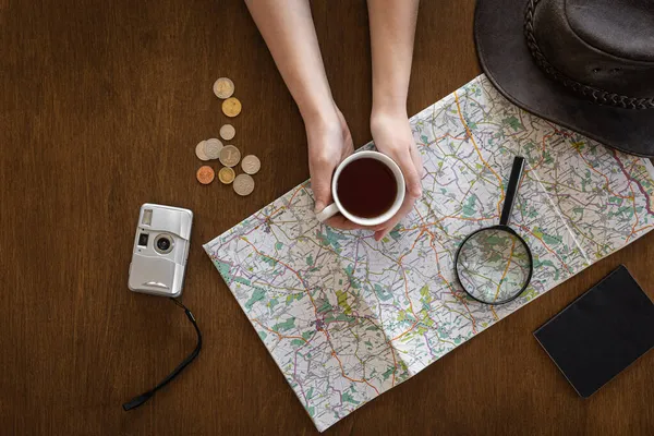 Platt läggning, karta, förstoringsglas, dokument och en kopp kaffe i händerna på en kvinna. — Stockfoto