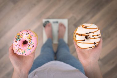 Bir kadın terazinin üzerinde duruyor, elinde donutlar, üst görünüm, kopyalama alanı.