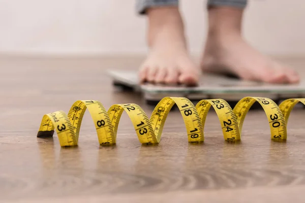 Female leg stepping on weigh scales with measuring tape. — Stock Photo, Image