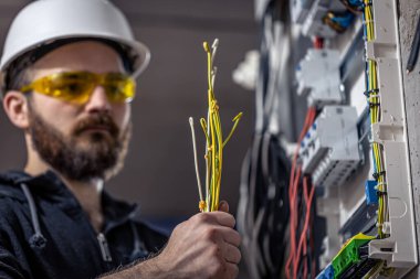 Bir erkek elektrikçi elektrik kablosuyla santralde çalışıyor..