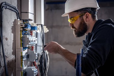 Bir erkek elektrikçi elektrik kablosuyla santralde çalışıyor..