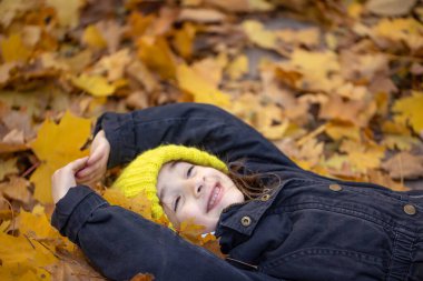 Sarı şapkalı küçük bir kız sonbahar yapraklarında yatıyor..