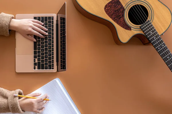 Musikalisk bakgrund med akustisk gitarr, laptop och kvinnliga händer, ovanifrån. — Stockfoto