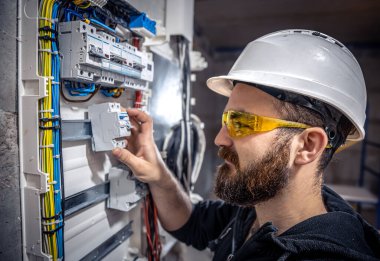 Bir erkek elektrikçi elektrik kablosuyla santralde çalışıyor..
