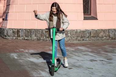Şehirde elektrikli scooter kullanan mutlu genç bir kadın..