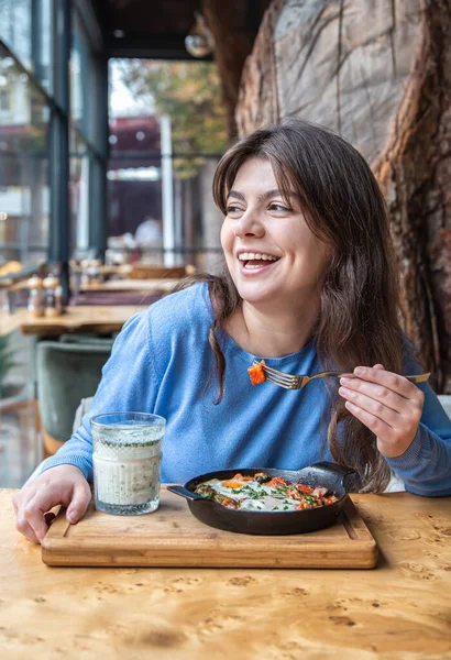 Una joven en un café cena en shakshuka tradicional y ayran. — Foto de Stock