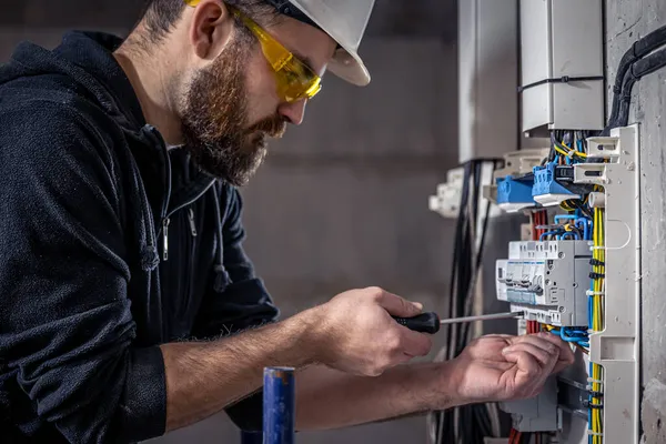 オスの電気技師は電気接続ケーブルのあるスイッチボードで働いています. — ストック写真