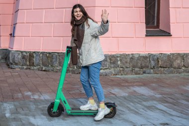 Şehirde elektrikli scooter kullanan mutlu genç bir kadın..