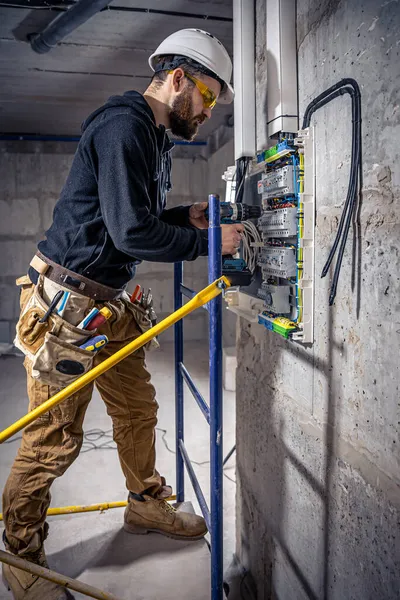 Un elettricista maschio lavora in un centralino con un cavo di collegamento elettrico . — Foto Stock