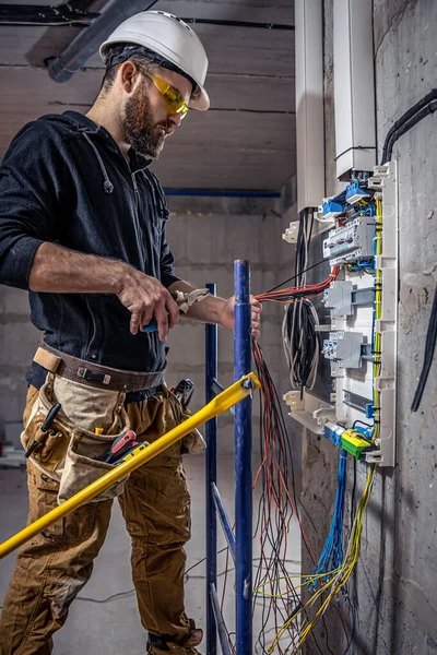 オスの電気技師は電気接続ケーブルのあるスイッチボードで働いています. — ストック写真