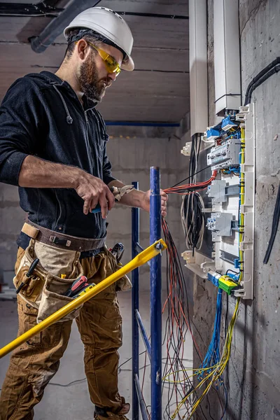 A male electrician works in a switchboard with an electrical connecting cable.