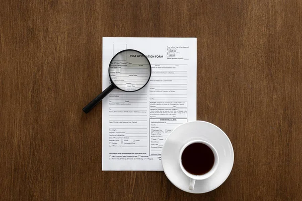 Visa application form, magnifier and a cup of coffee on a wooden background.
