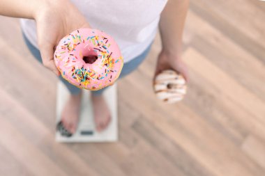 Bir kadın terazinin üzerinde duruyor, elinde donutlar, üst görünüm, kopyalama alanı.
