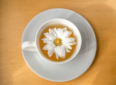 Tahta arka planda papatya çiçeği olan bir fincan çay, yakın plan..