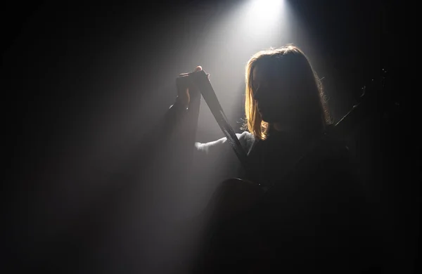 Flicka med akustisk gitarr i mörkret under en ljusstråle. — Stockfoto