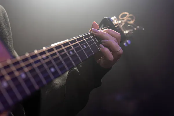 Närbild av kvinnliga händer som spelar akustisk gitarr i mörkret. — Stockfoto