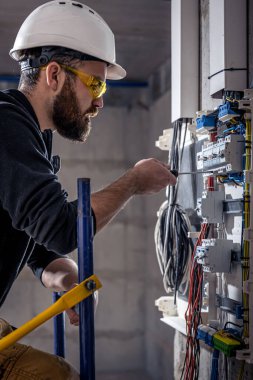 Bir erkek elektrikçi elektrik kablosuyla santralde çalışıyor..