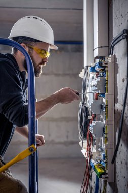 Bir erkek elektrikçi elektrik kablosuyla santralde çalışıyor..