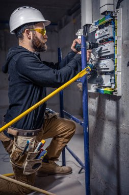 Bir erkek elektrikçi elektrik kablosuyla santralde çalışıyor..