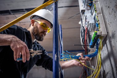 Bir erkek elektrikçi elektrik kablosuyla santralde çalışıyor..