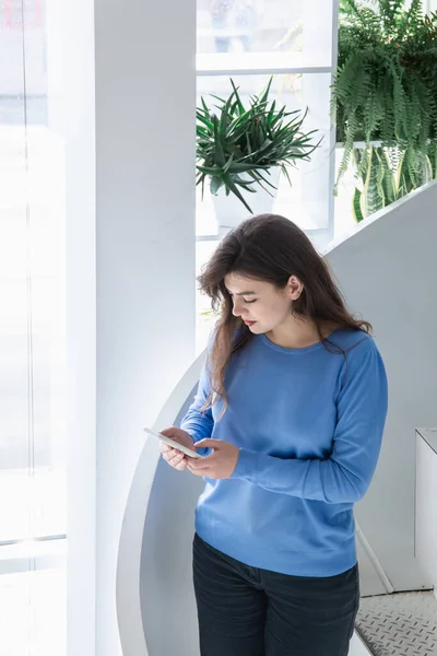 Mujer joven atractiva en un suéter azul utiliza el teléfono. — Foto de Stock