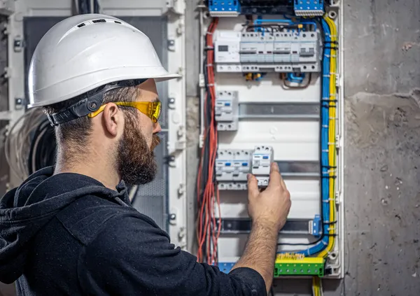 A male electrician works in a switchboard with an electrical connecting cable.