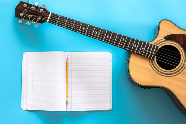 Akustisk gitarr och anteckningsblock på en blå bakgrund, ovanifrån. — Stockfoto