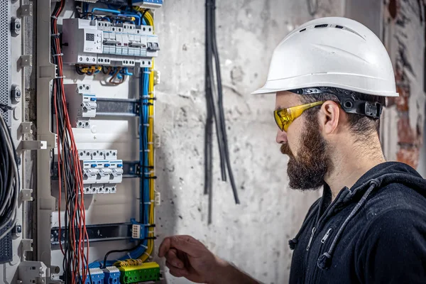 A male electrician works in a switchboard with an electrical connecting cable.