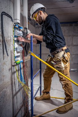 Bir erkek elektrikçi elektrik kablosuyla santralde çalışıyor..