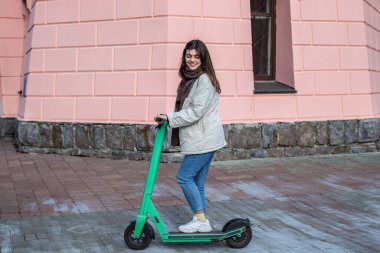 Şehirde elektrikli scooter kullanan mutlu genç bir kadın..
