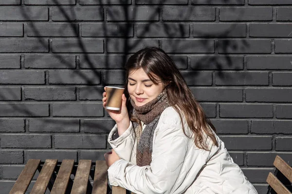 Mujer joven disfrutando de una bebida contra la pared de ladrillo de la cafetería exterior. — Foto de Stock