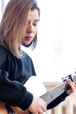 Ciddi bir genç kadın evde akustik gitar çalıyor..