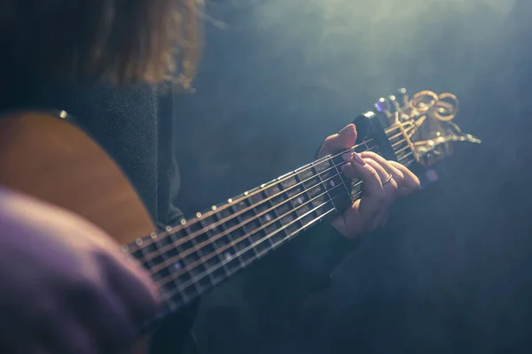 Ung kvinna spelar akustisk gitarr i ett mörkt rum med dis. — Stockfoto