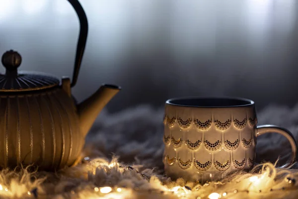 Tekanna och kopp på en suddig bakgrund i mörkret med girlanger. — Stockfoto