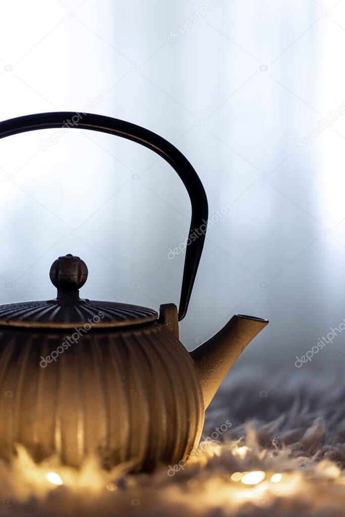 Teapot on a blurred background in the dark with garlands.