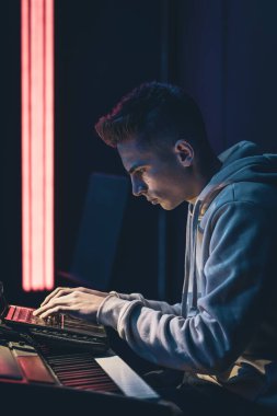 Karanlık bir odada, müzik anahtarlarının başında dizüstü bilgisayarlı genç bir adam..