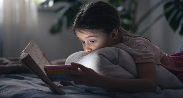Ein kleines Mädchen telefoniert mit einem Buch in der Hand. — Stockfoto