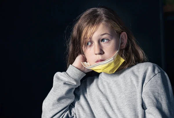 Fetiță tristă într-o mască medicală galbenă pe un fundal negru. — Fotografie, imagine de stoc