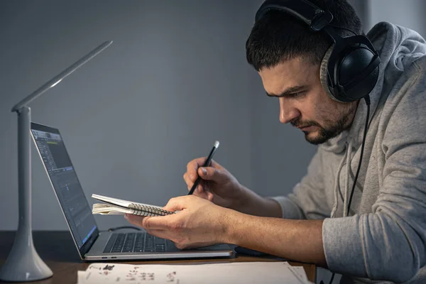 Un hombre con auriculares en la noche delante de una pantalla de ordenador portátil escribe música. — Foto de Stock