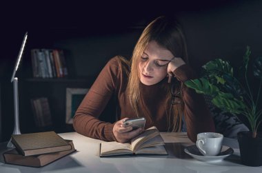 Genç bir kadın masada oturur ve gece lambasıyla kitap okur..