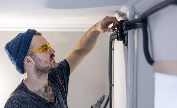 An electrician is mounting electric sockets on the white wall indoors. — Stock Photo, Image