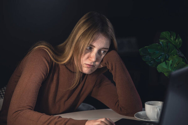 Молодая женщина работает ночью за ноутбуком с лампой.