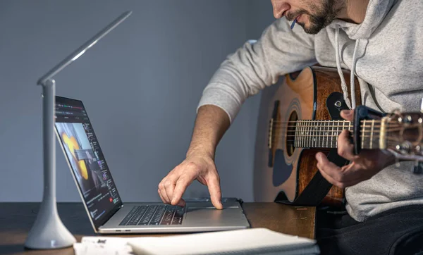Un hombre con una guitarra delante de un portátil a última hora aprende a tocar. — Foto de Stock