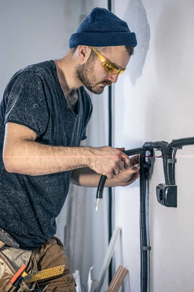 En elektriker monterer elektriske stikkontakter på den hvide væg indendørs. - Stock-foto