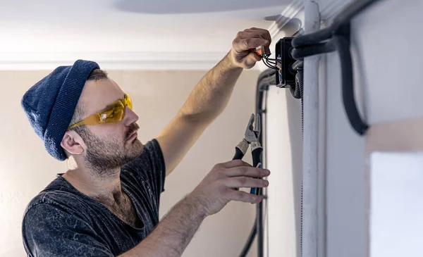 An electrician is mounting electric sockets on the white wall indoors. — Stock Photo, Image