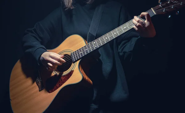 Une jeune femme avec une guitare acoustique dans le noir sous un rayon de lumière. — Photo