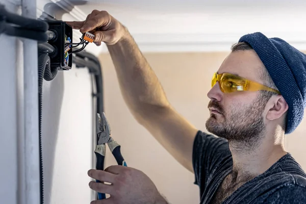 An electrician is mounting electric sockets on the white wall indoors. — Stock Photo, Image