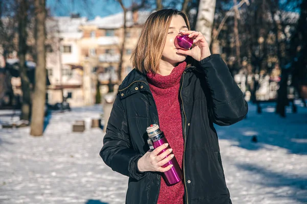 O tânără bea băutură fierbinte cu termos într-o zi însorită de iarnă. — Fotografie, imagine de stoc