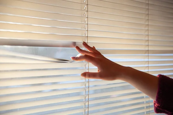 Womans hand taking a peak through the window blinds.